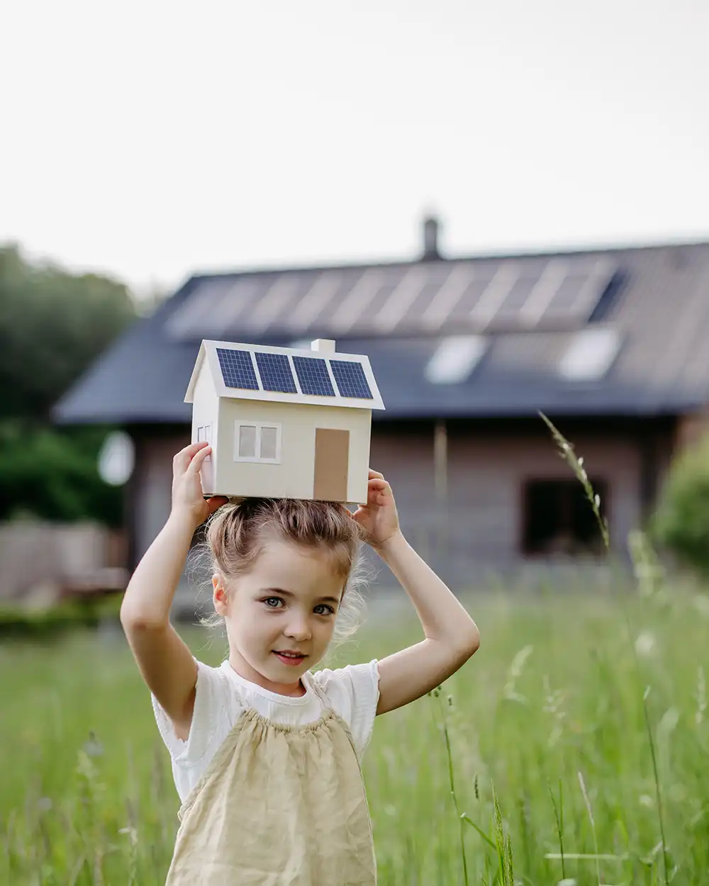 Porträt eines kleinen Mädchens, das ein Modell eines Hauses mit Sonnenkollektoren hält, Konzept des nachhaltigen Lebensstils und der erneuerbaren Ressourcen.