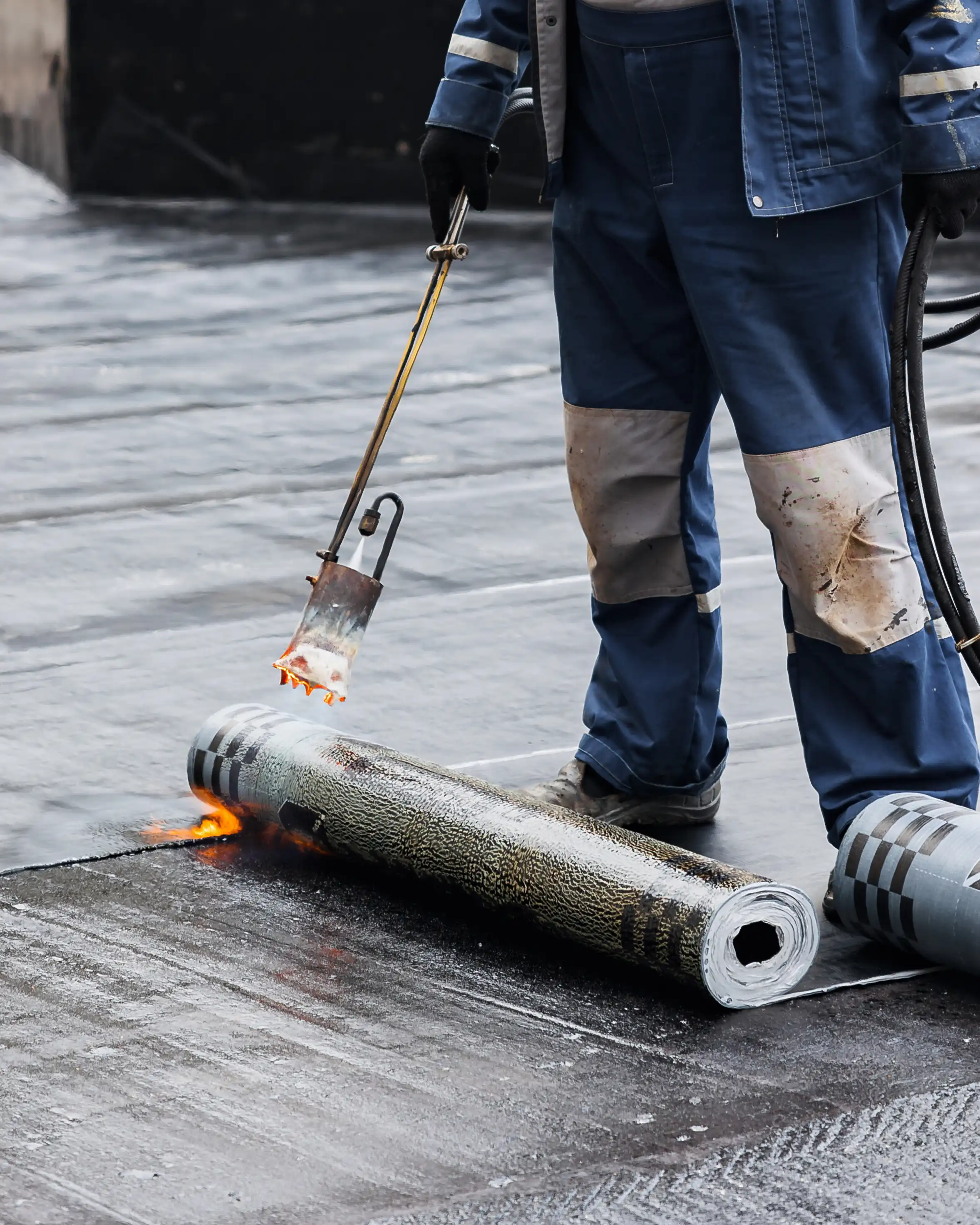 Rolldachabdichtung von Betonplatten aus Stylobat. Verlegung mit Propangasbrenner während der Bauarbeiten. Verlegung von Flachdächern. Erhitzen und Schmelzen von Bitumendachpappe.